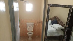 A small bathroom with a toilet, a mirror, and a bed visible in the reflection.