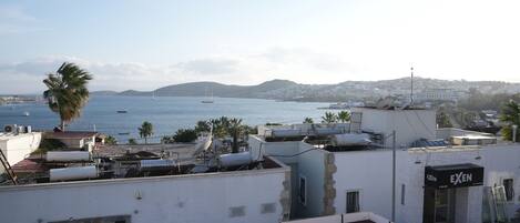 Un bâtiment situé sur la côte, doté d’une terrasse sur le toit, d’une façade visible et offrant une vue sur la mer et les collines lointaines.