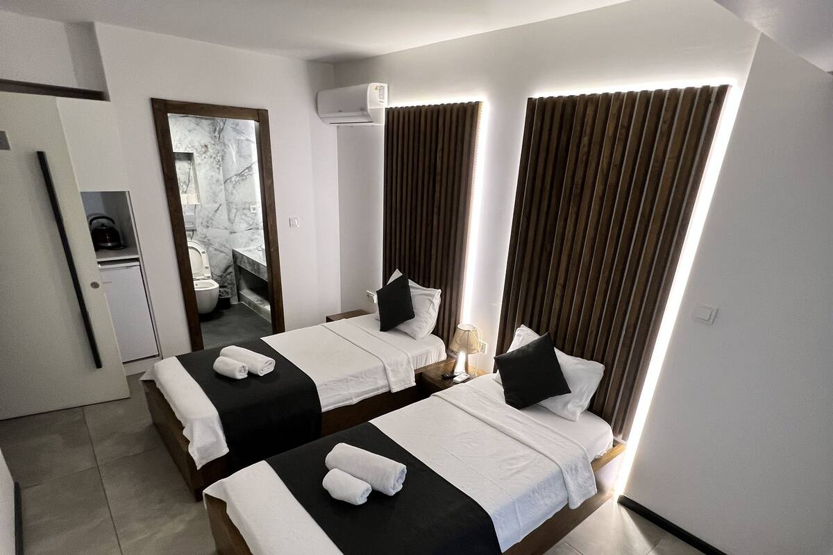 Una habitación de hotel moderna con dos camas, baño y una pequeña cocina.