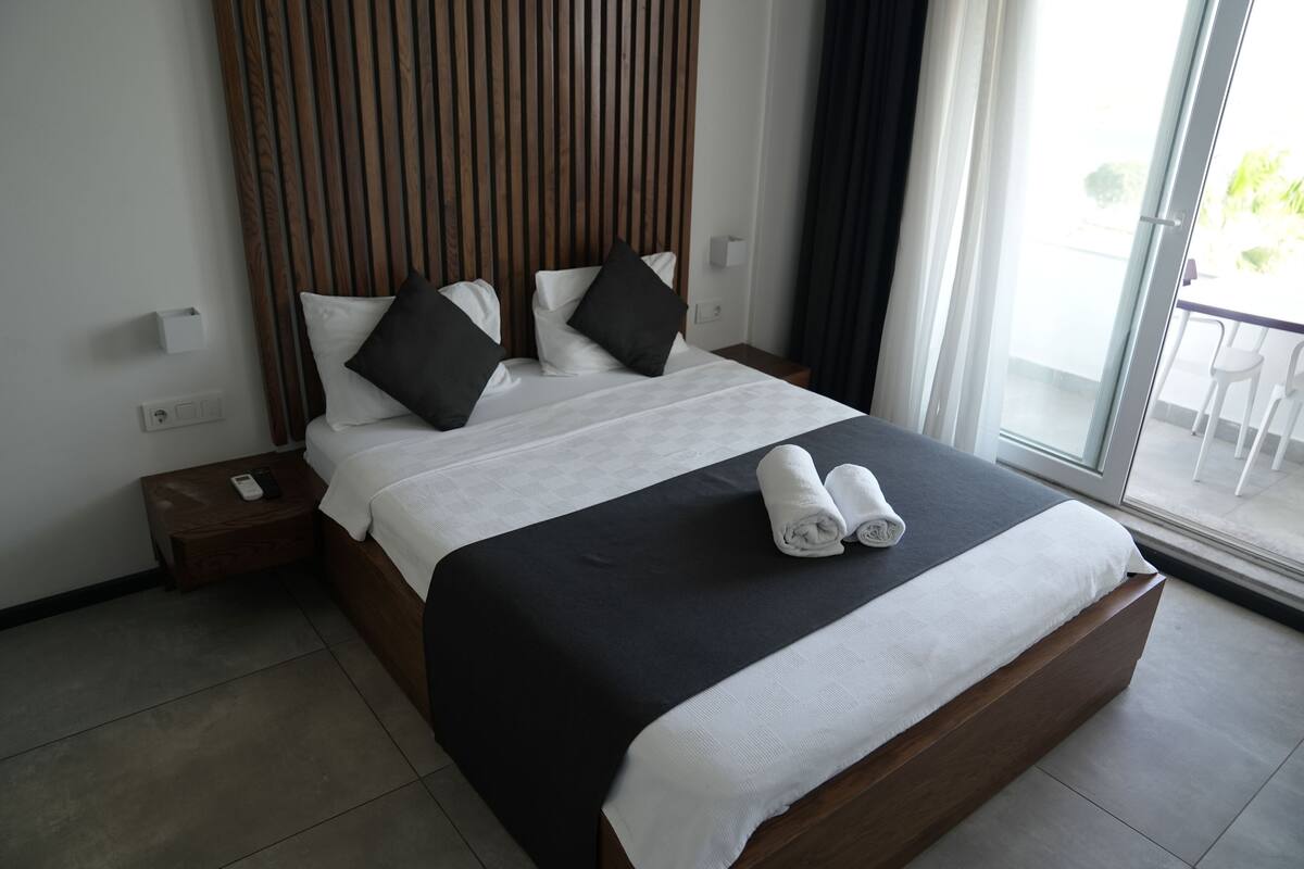 Habitación de hotel moderna con una cama grande, cabecera de madera y vistas al exterior.