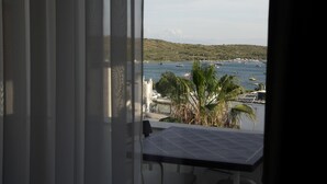 Un balcon offrant une vue sur un port de plaisance, des palmiers et un paysage vallonné.