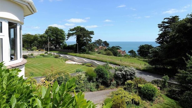 A coastal property with a curved driveway, lush greenery, and a view of the sea. - Westdale Edge (Seaton)