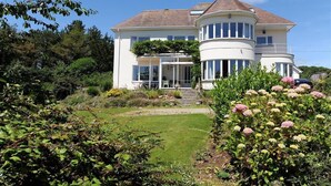 A two-story house with a curved roof, a front porch, and a well-maintained garden with various plants and flowers. - Westdale Edge (Seaton)