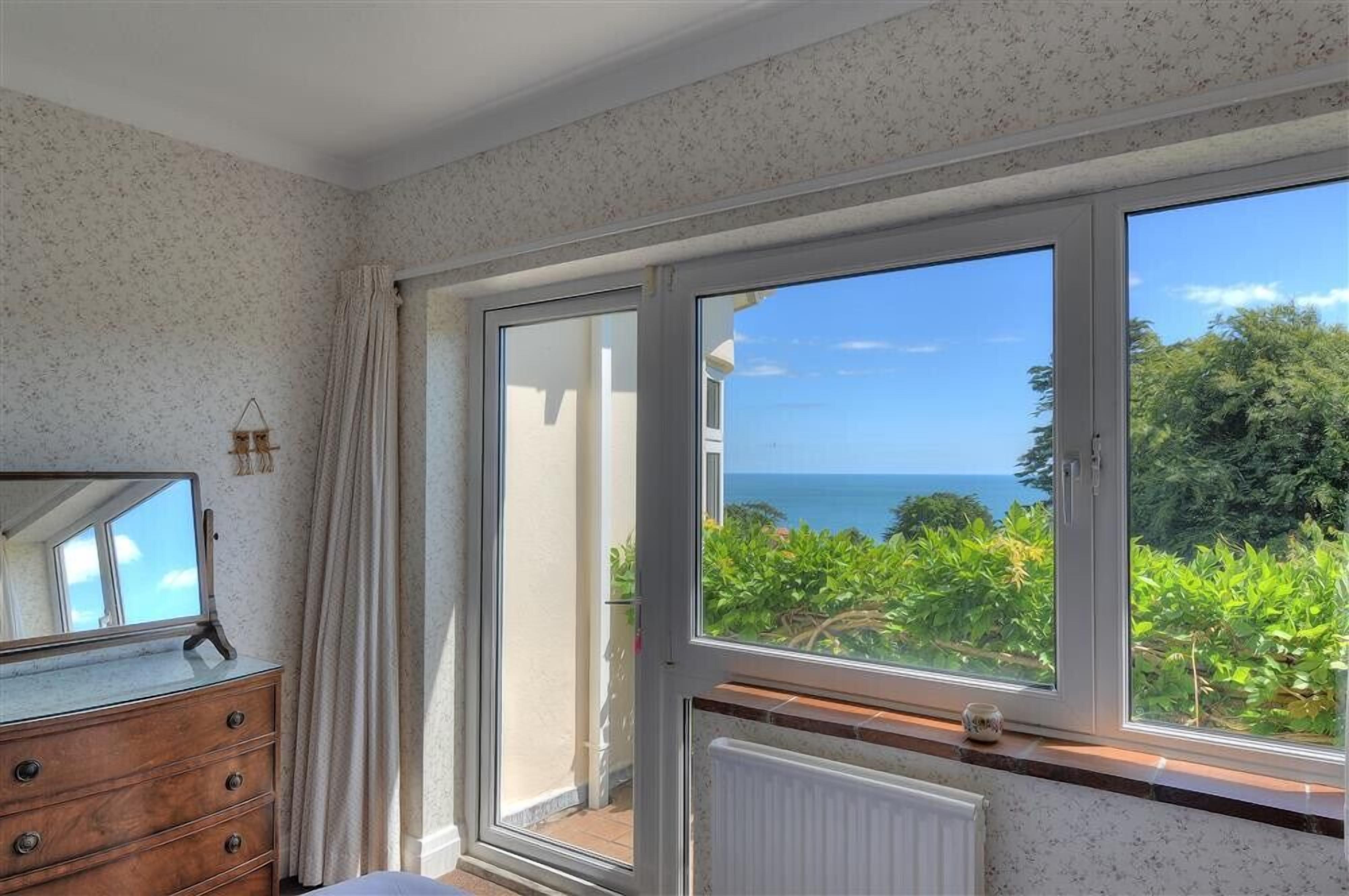 A room with a large window offering a view of the sea and greenery.