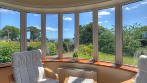 A room with a curved bay window overlooking a lush garden and a clear blue sky. - Westdale Edge (Seaton)