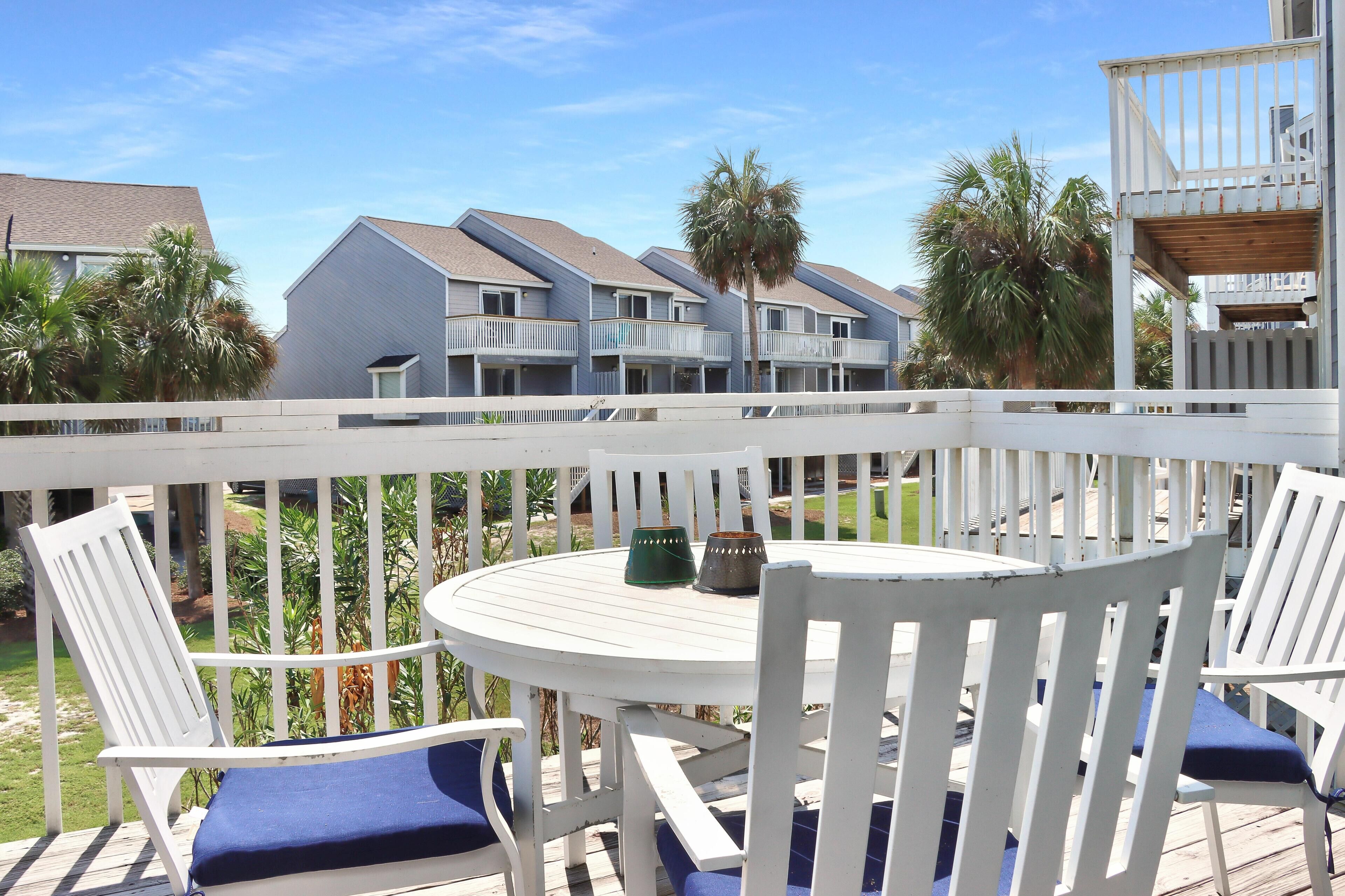 A deck with white railings, a round table, and blue cushioned chairs.