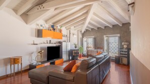 Un vaste espace de vie comprenant un grand canapé, un téléviseur à écran plat et un coin cuisine avec un meuble de couleur orange.