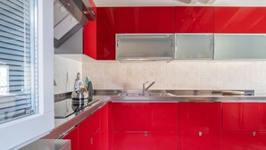 Une cuisine moderne avec des meubles de rangement rouges, un évier en acier inoxydable et une fenêtre équipée de stores.