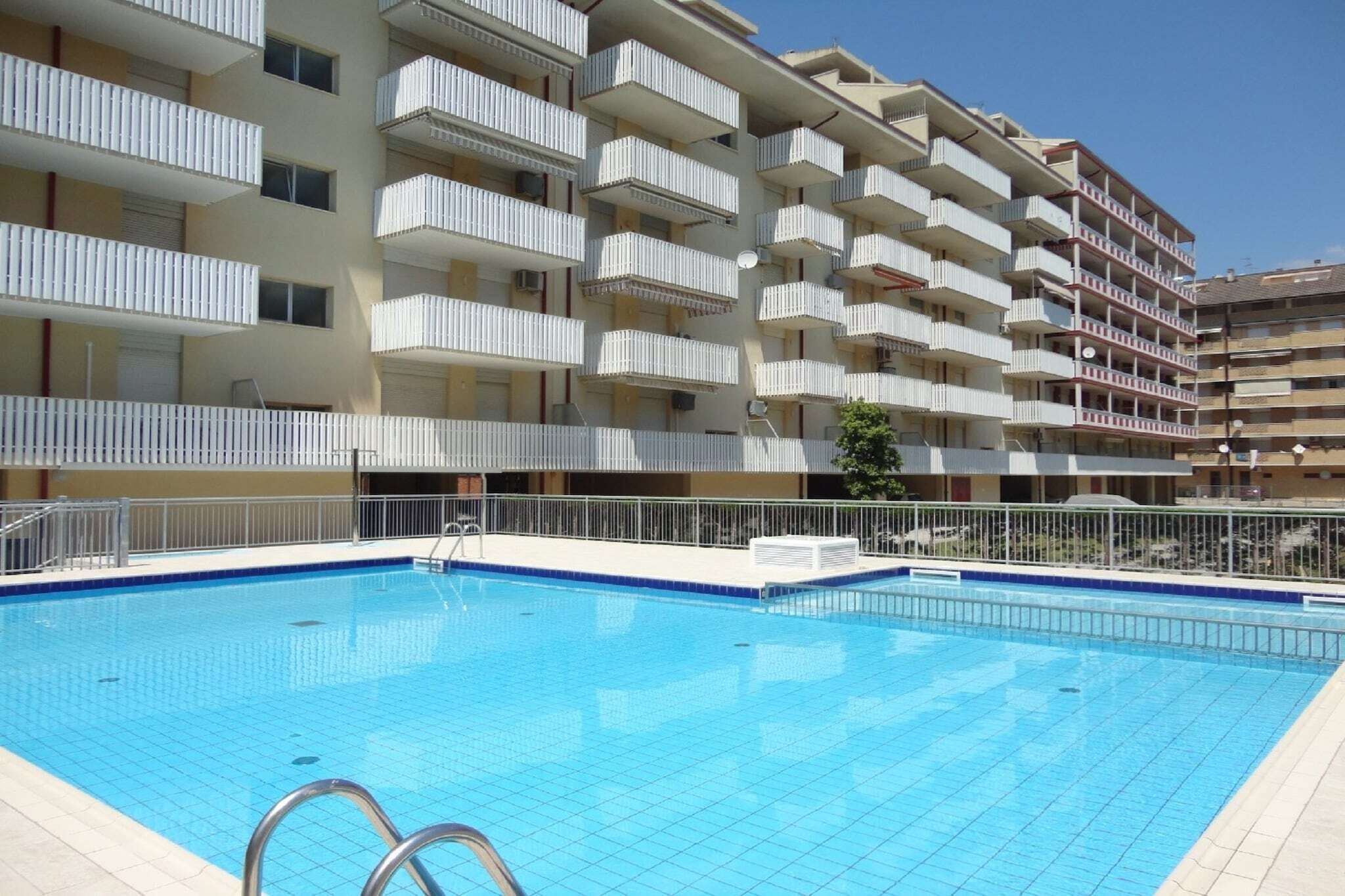Une piscine dotée d’une terrasse carrelée, entourée d’un immeuble à plusieurs étages avec des balcons.