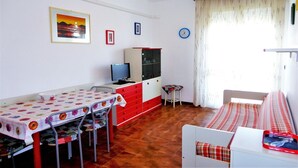 Una habitación con una mesa de comedor, sillas, un televisor, un armario, una cama y una ventana con cortinas.