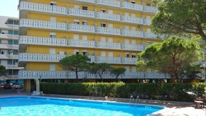 Un hotel con piscina, varios balcones y un árbol en primer plano.