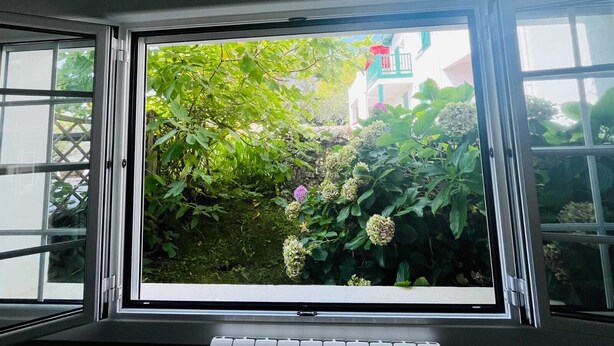 A room with a large window overlooking a garden with various plants and flowers. - COTE BASQUE BIDART Apt, terrace, gardin, BBQ, Surf, near beach, all shops  (Bidart)