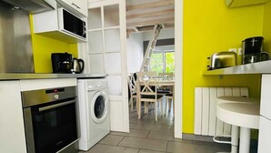 A compact kitchen with a washing machine, a microwave, and a stove. A dining area with a table and chairs is visible through an open doorway. - COTE BASQUE BIDART Apt, terrace, gardin, BBQ, Surf, near beach, all shops  (Bidart)