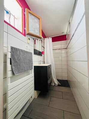 A small bathroom with white tiled walls, a black sink, a mirror, a towel, and a shower curtain. - COTE BASQUE BIDART Apt, terrace, gardin, BBQ, Surf, near beach, all shops  (Bidart)