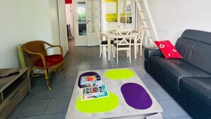 A modern living room with a loft-style ceiling, a wooden coffee table with magazines, a black sofa, and a wicker chair. - COTE BASQUE BIDART Apt, terrace, gardin, BBQ, Surf, near beach, all shops  (Bidart)