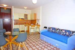 A compact living space with a kitchenette, a dining area with a glass table, and a sofa with patterned cushions.
