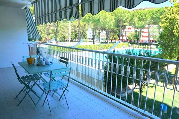 A balcony with a table and chairs, a view of a swimming pool, and a building in the background.