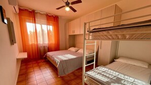 A room with a bunk bed, a single bed, a ceiling fan, and a window with curtains. - Apartment in Porto Santa Margherita (VE) (Porto Santa Margherita (VE))