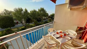 A balcony with a pool view, white plastic chairs, and a table set for two. - Apartment in Porto Santa Margherita (VE) (Porto Santa Margherita (VE))