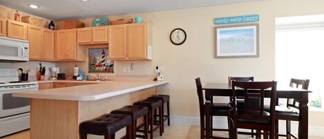 A kitchen with wooden cabinets, a central island with stools, a microwave, and a clock on the wall.