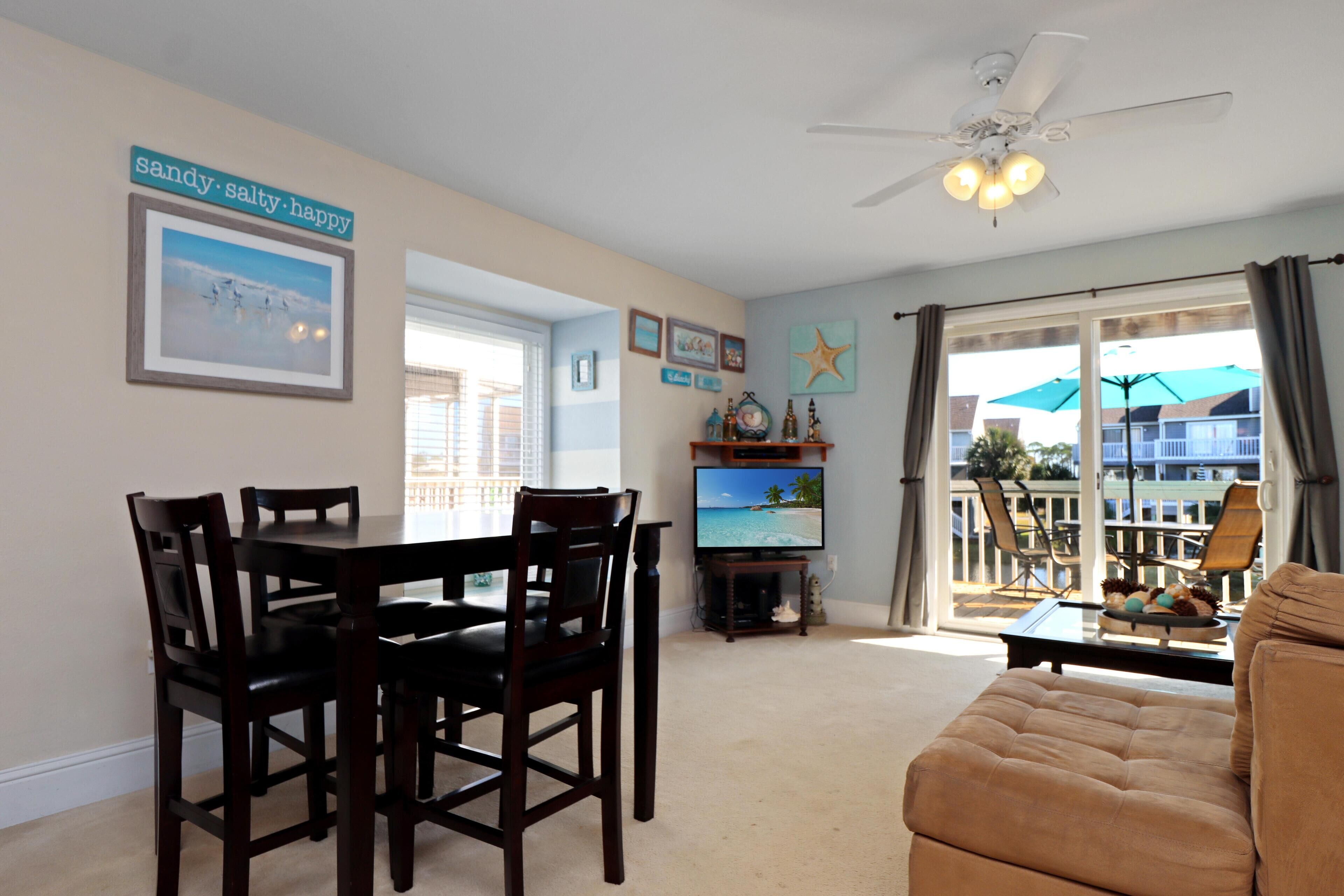 A dining area with a table and chairs, a television, and a balcony with outdoor furniture.