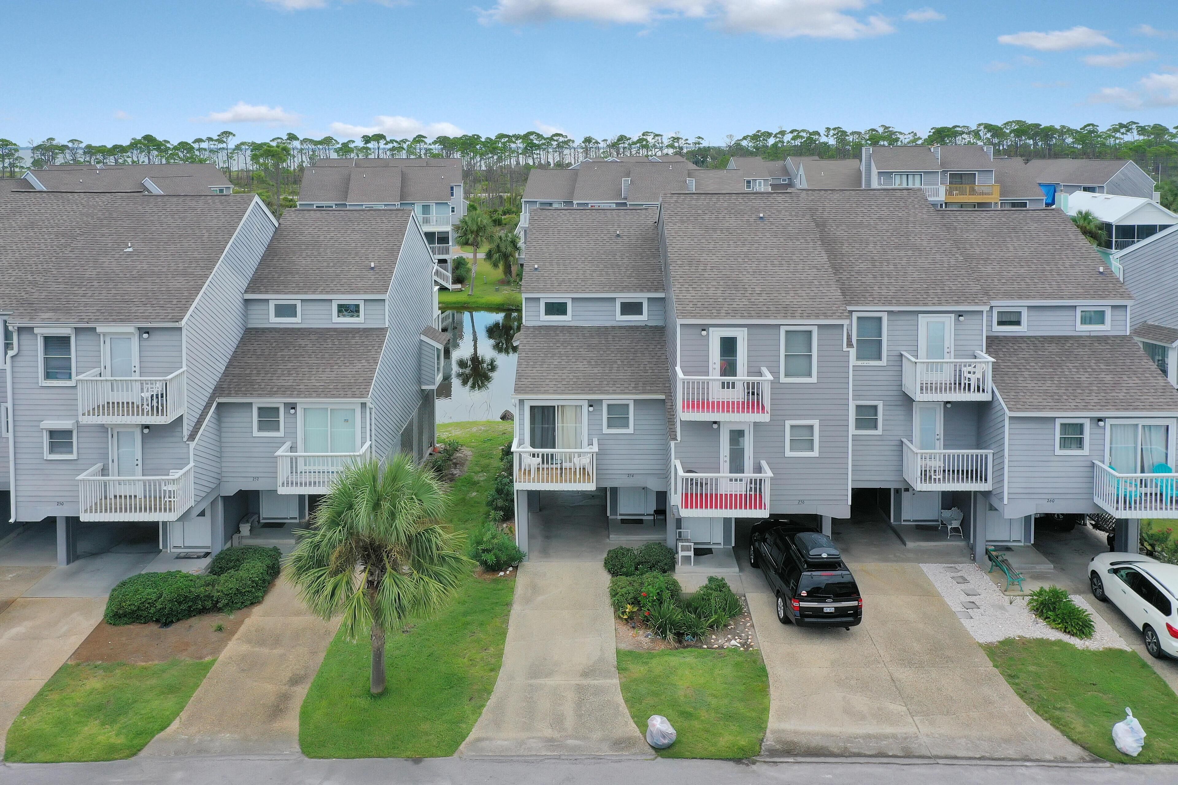 A row of two-story townhouses with balconies, a small lawn, and a parked car.