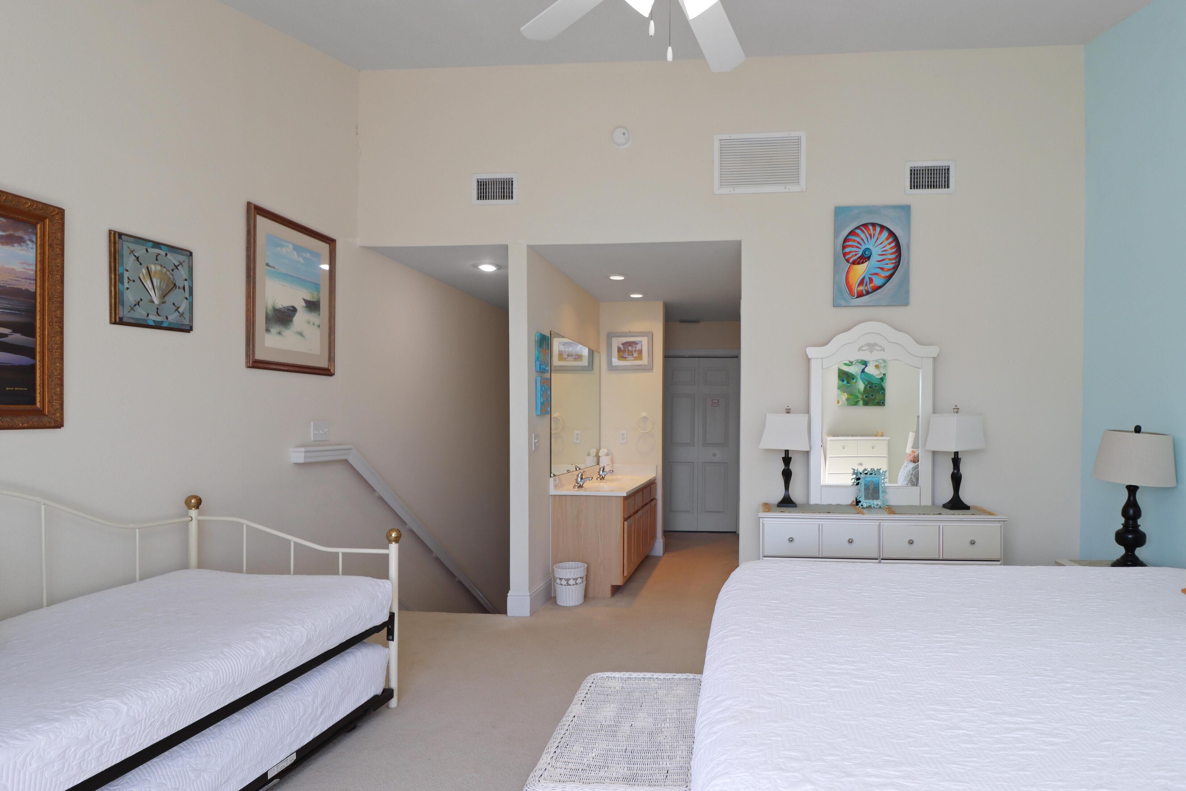 A bedroom with two beds, a bathroom, and a staircase leading to another room.