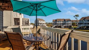 A balcony with a glass table and chairs, a green umbrella, and a view of adjacent buildings. - Barrier Dunes 254 - 108 (Port St. Joe)