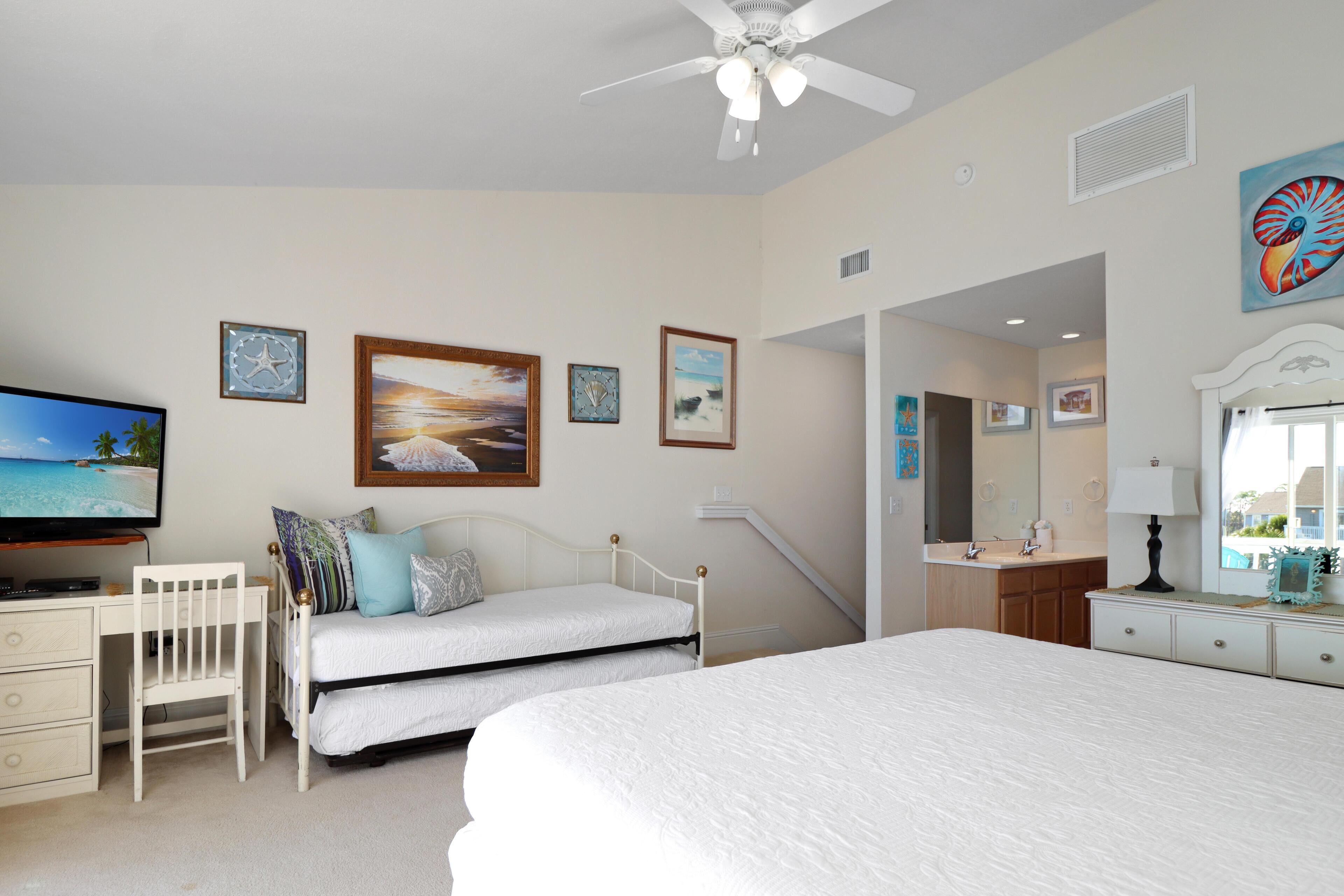 A bedroom with a large bed, a smaller bed, a desk, a chair, a TV, and artwork on the walls.