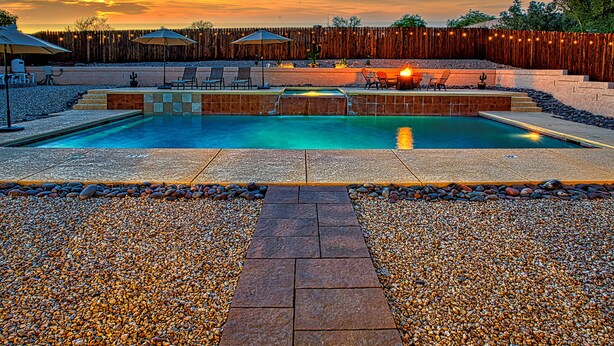Una piscina con borde de piedra, rodeada de piedras y una valla de madera.