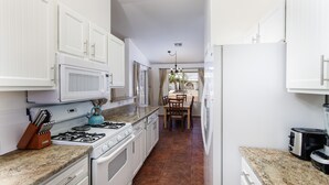 Una cocina con armarios blancos, encimera de granito, estufa a gas y microondas.
