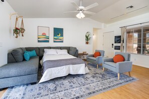 A modern bedroom with a bed, grey sofa, armchair, and a ceiling fan. - Splash into this Huge Havasu Pool and Spa! King bed! (Lake Havasu City)