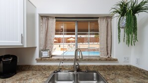 Una cocina con un lavamanos doble, una cafetera y ventana con vista a una piscina.