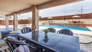 Un patio al aire libre con una mesa y sillas de comedor, una piscina y una cerca de madera al fondo.