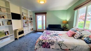 Un dormitorio con cama, una estantería, una silla y ventana con vistas.