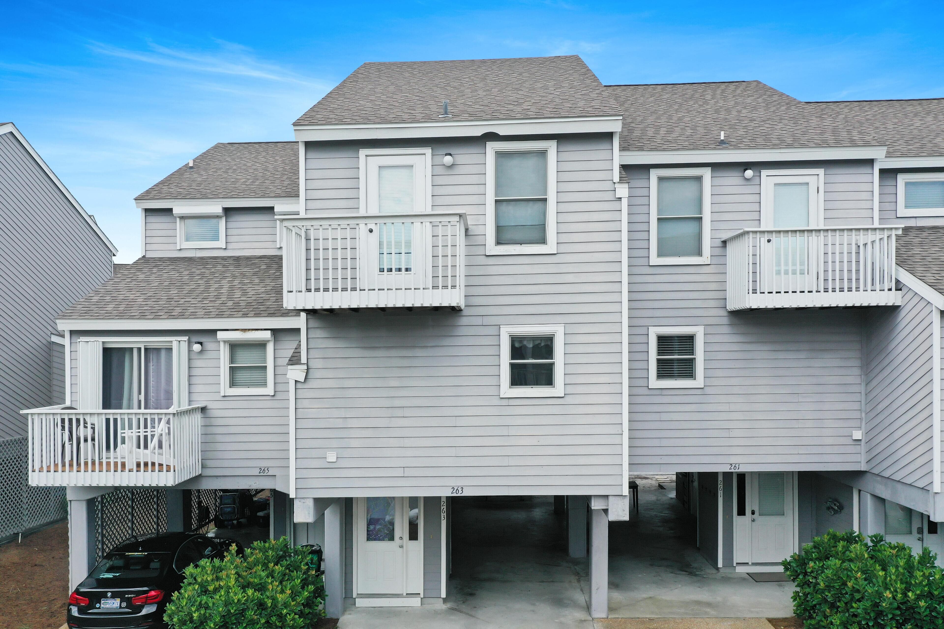 A multi-story residential building with a garage entrance, a balcony on the second floor, and a small porch area.
