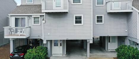 A multi-story residential building with a garage entrance, a balcony on the second floor, and a small porch area.