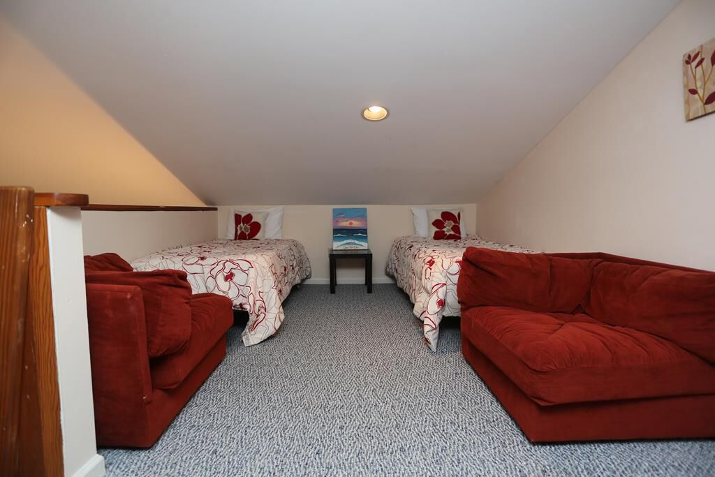 Une petite chambre accueillante, avec deux lits simples, un canapé rouge et une petite table placée au centre.