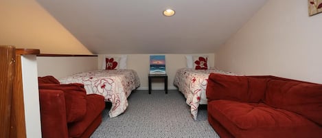 Une petite chambre accueillante, avec deux lits simples, un canapé rouge et une petite table placée au centre.