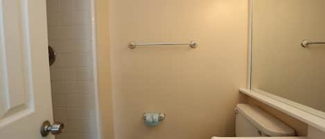 A bathroom with a toilet, a shower, a towel rack, and a trash bin.