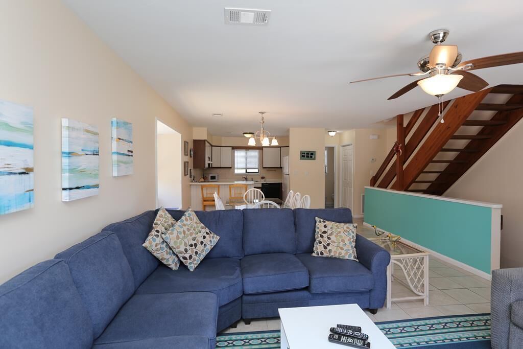 A living room with a blue sofa, a coffee table, and a ceiling fan. There is a staircase leading to an upper level.