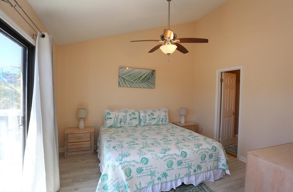 A bedroom with a bed, two bedside tables, a ceiling fan, a window with curtains, and a door.