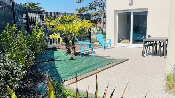 A backyard with a pool, a covered patio area, and a small garden with plants and a palm tree. - Gîte 10pers Avec Jacuzzi & Sauna Privatifs (Blainville-sur-Mer)
