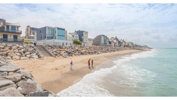 Una playa con costa rocosa, algunas personas caminando y edificios a lo largo de la costa.