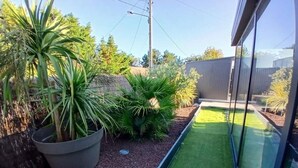 Un pequeño patio trasero con diversas plantas, un cerco de madera y un cielo despejado.