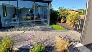 Una casa moderna con un invernadero de vidrio, un patio con plantas y un jardín bien cuidado.