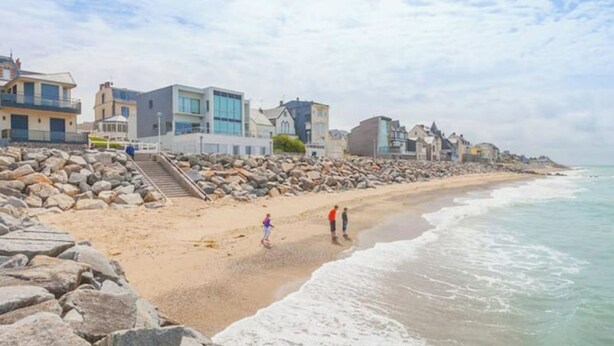 Una playa con costa rocosa, algunas personas caminando y edificios a lo largo de la costa.