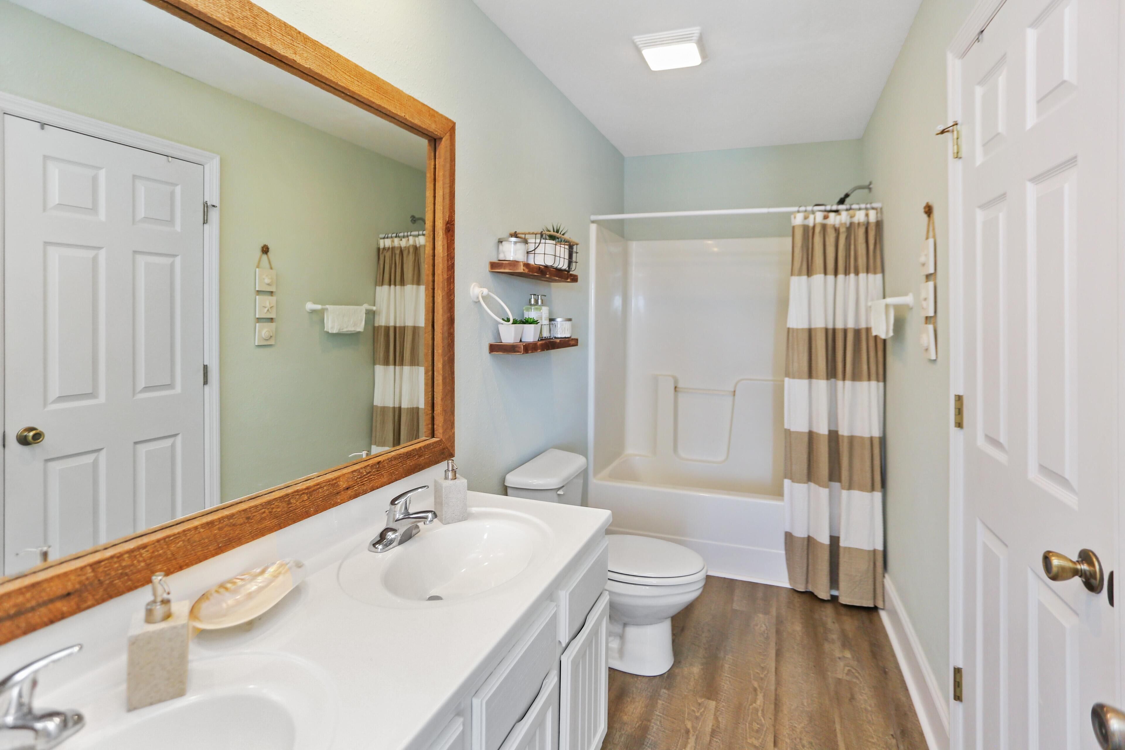 A bathroom with a white sink, a toilet, a bathtub, and a shower. There are wooden shelves above the sink and a mirror with a wooden frame.