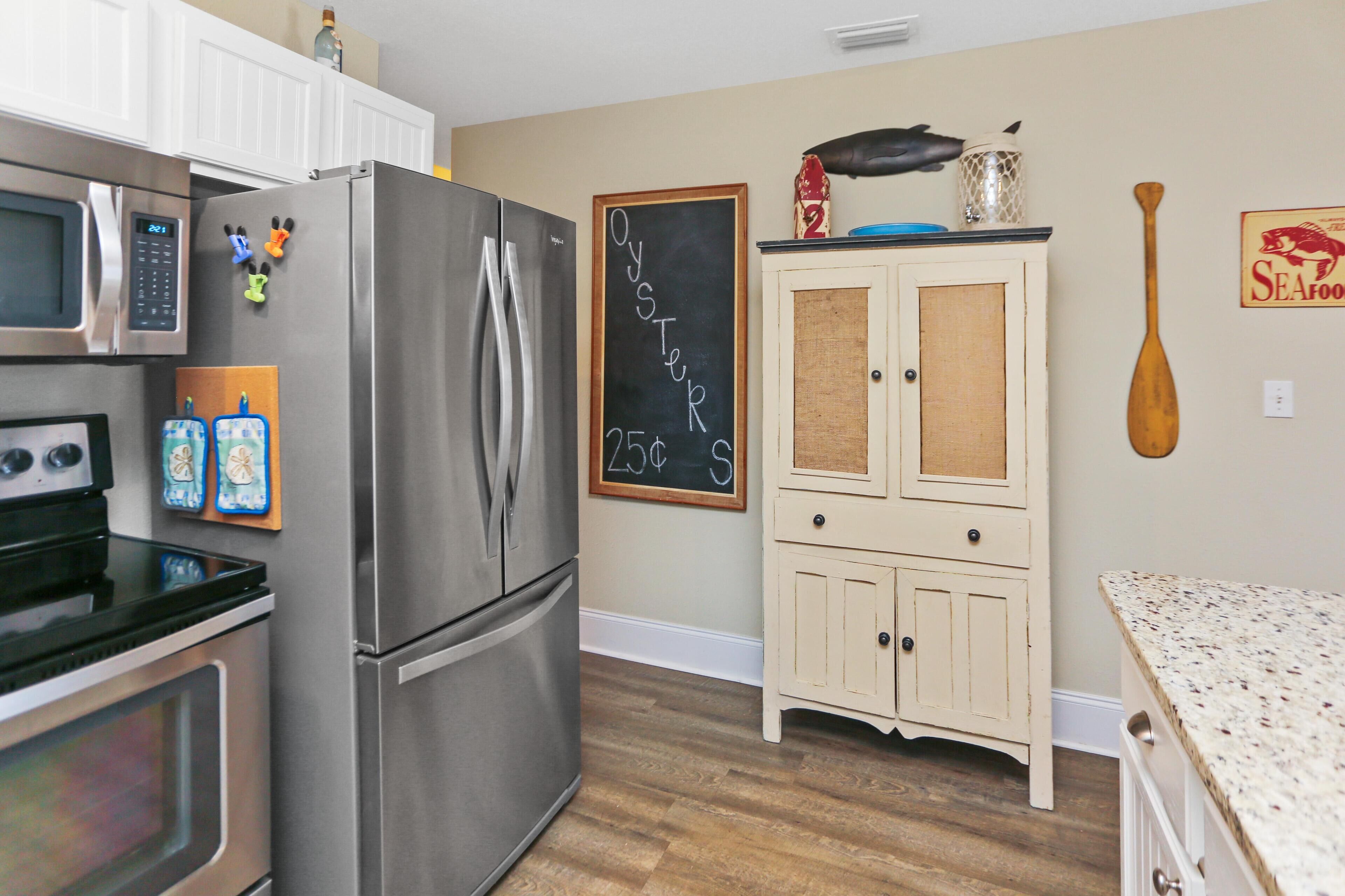 A kitchen with a stainless steel refrigerator, a microwave, and an oven. There is a chalkboard with 'OYSTER' written on it.