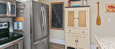 A kitchen with a stainless steel refrigerator, a microwave, and an oven. There is a chalkboard with 'OYSTER' written on it.